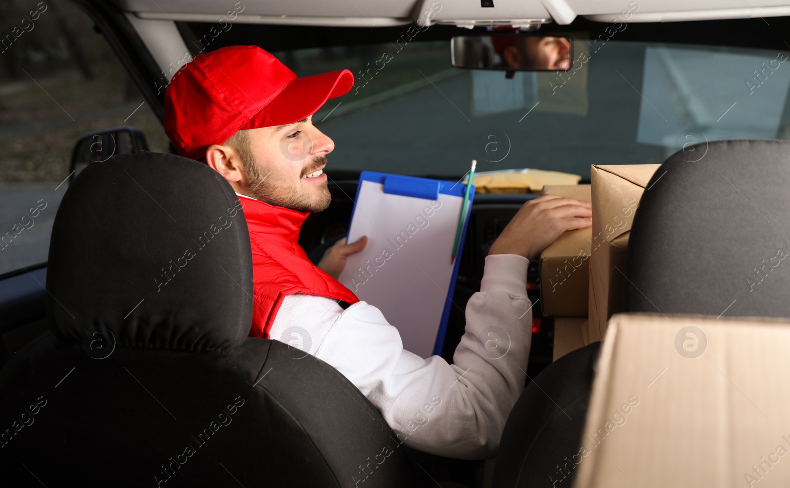 Photo of Deliveryman with clipboard and parcels in car