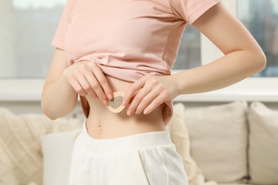 Photo of Woman applying contraceptive patch onto her body indoors, closeup