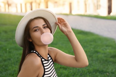 Photo of Beautiful woman in hat blowing gum on green grass outdoors