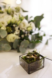 Beautiful wedding rings in glass box and flowers on textile surface