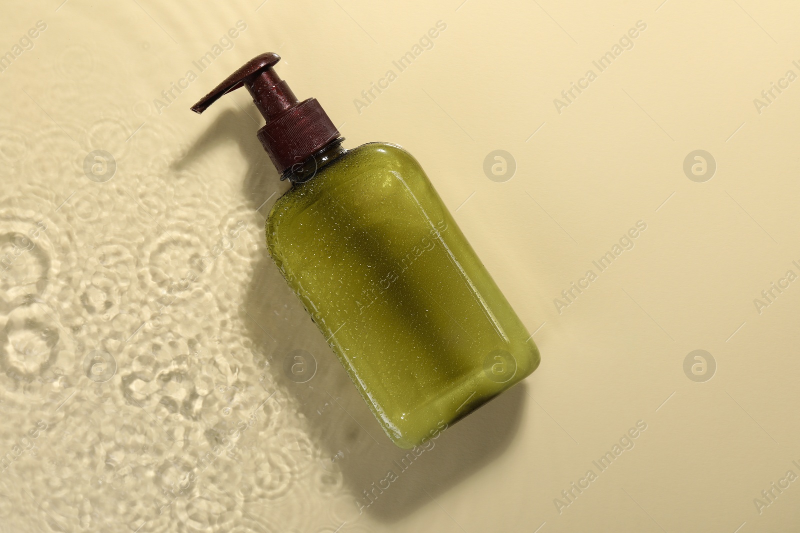 Photo of Bottle of face cleansing product in water against beige background, top view