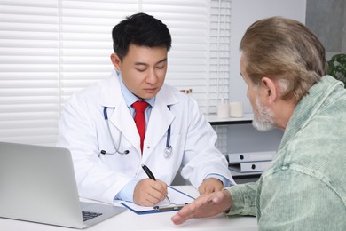 Photo of Doctor consulting senior patient at white table in clinic