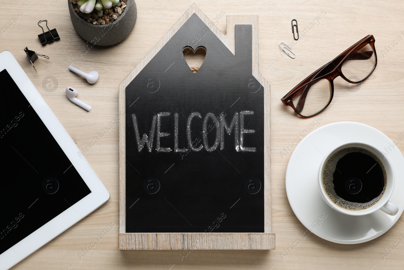 Photo of Flat lay composition of house shaped blackboard with word Welcome and gadgets on wooden table