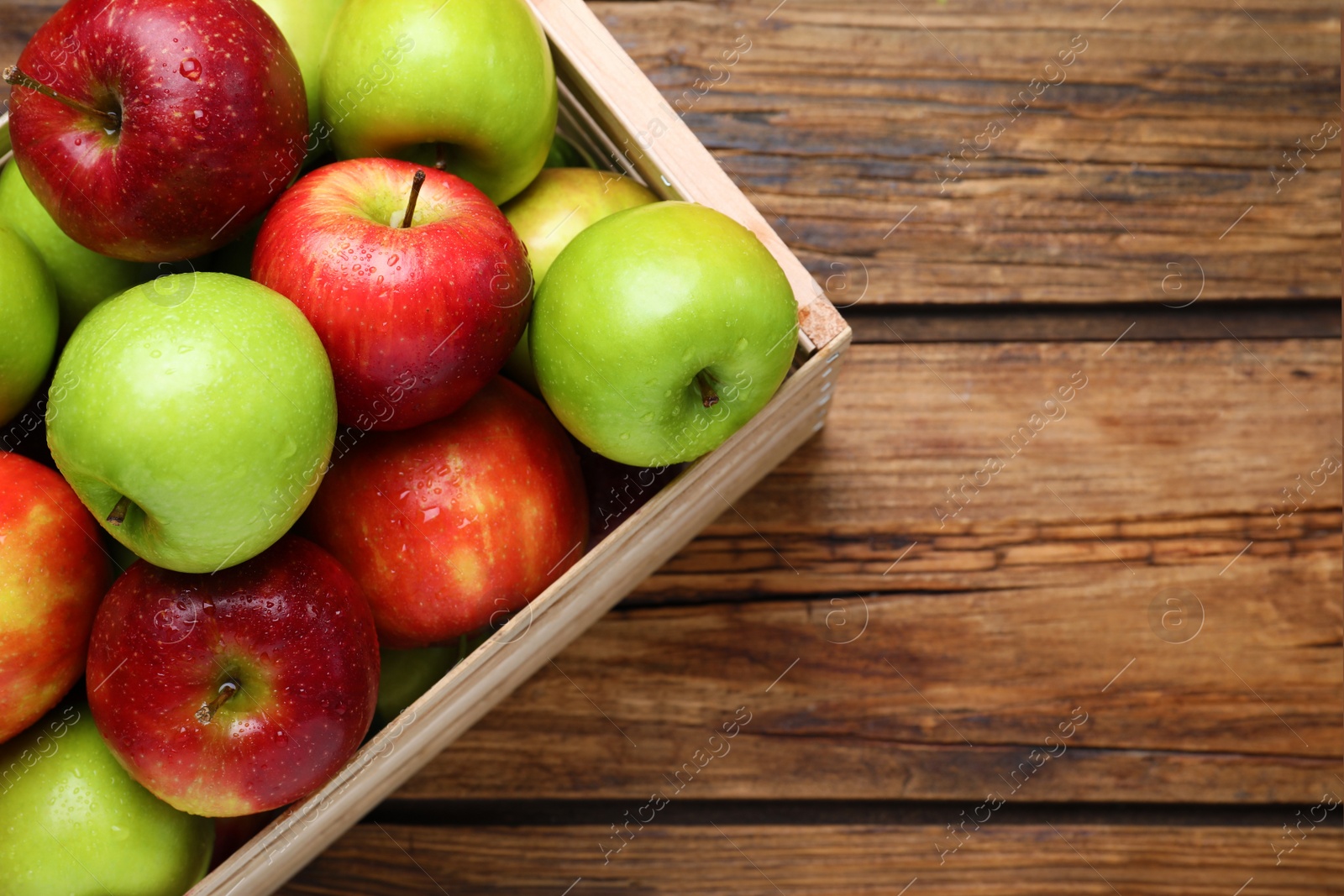 Photo of Ripe juicy apples in wooden crate on wooden table, top view. Space for text