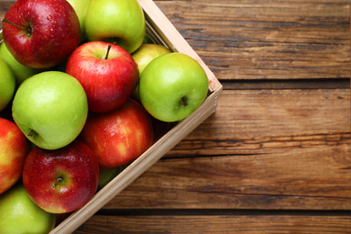 Ripe juicy apples in wooden crate on wooden table, top view. Space for text