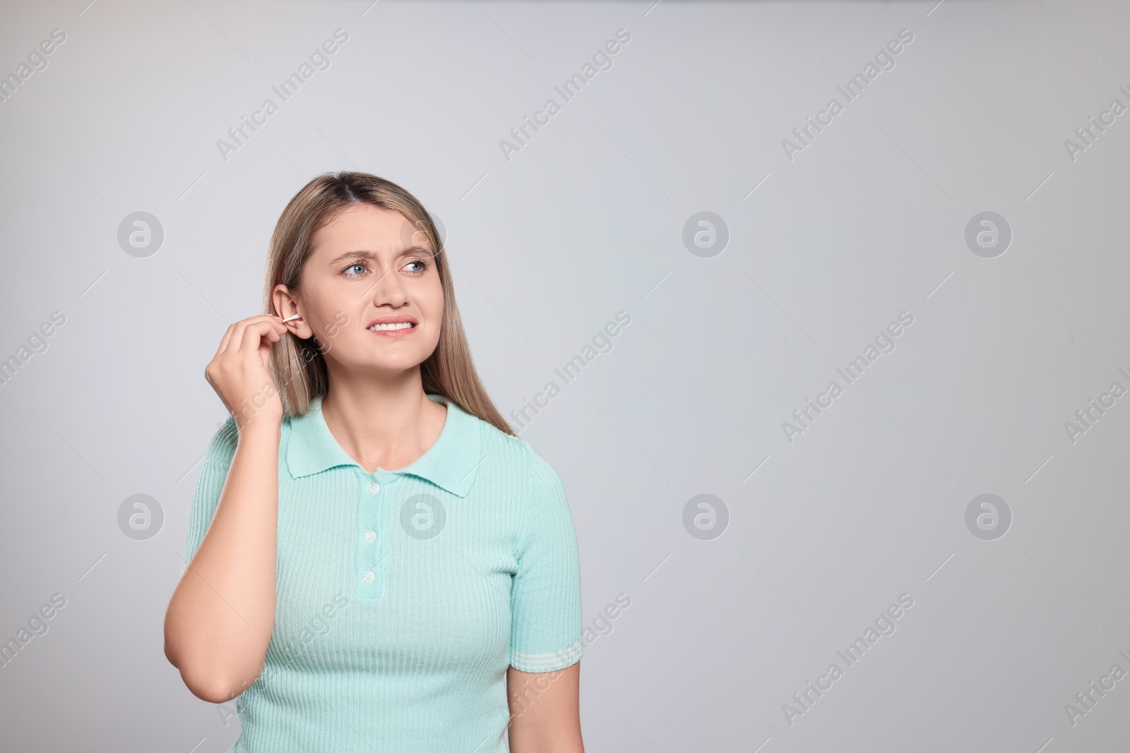 Photo of Young woman cleaning ear with cotton swab on light grey background. Space for text