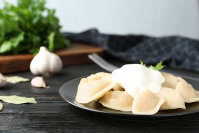 Photo of Delicious cooked dumplings with sour cream on dark wooden table