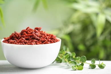 Photo of Bowl of dried goji berries on table against blurred background. Space for text