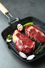 Photo of Grill pan with pieces of fresh beef meat, thyme and spices on gray table