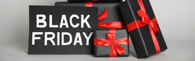 Many gift boxes and sheet of paper with words Black Friday on light grey background. Banner design