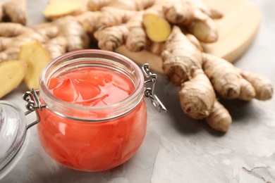 Photo of Spicy pickled ginger and root on light grey table, space for text