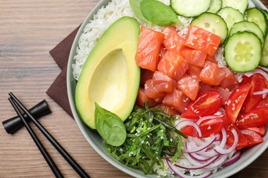Delicious poke bowl with salmon and vegetables served on wooden table, flat lay