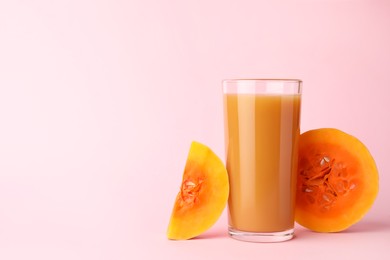 Photo of Tasty pumpkin juice in glass and cut pumpkin on pink background. Space for text