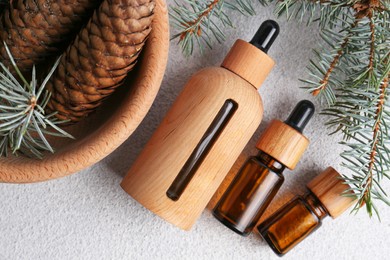Photo of Bottlesaromatic essential oil, pine branches and cones on light grey table, flat lay