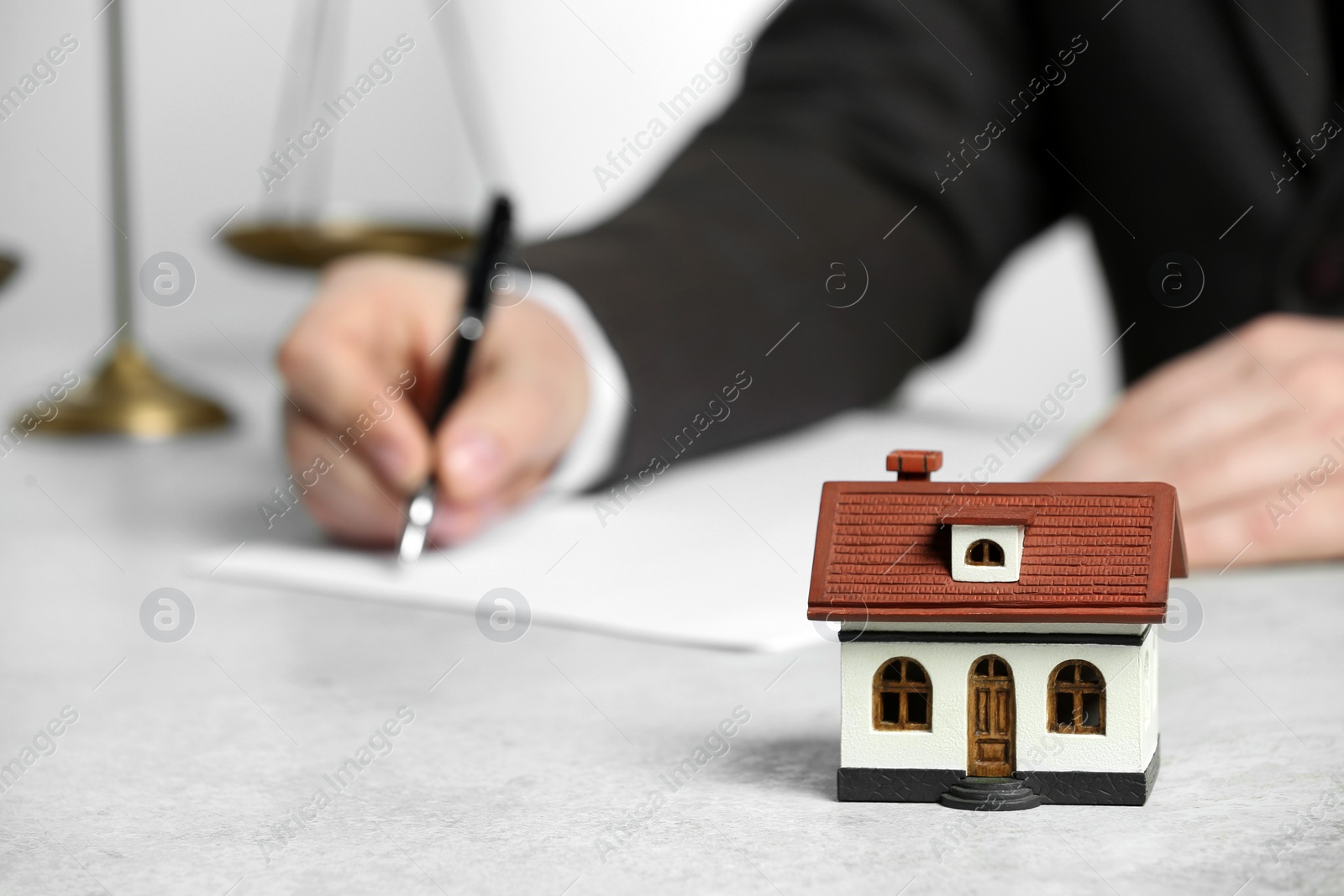 Photo of Construction and land law concepts. Man writing at white table, focus on house model