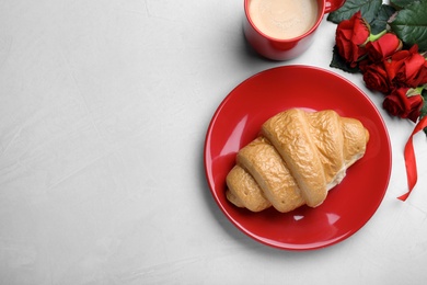 Cup of coffee, croissant and roses on light grey table, flat lay with space for text. Valentine's day breakfast