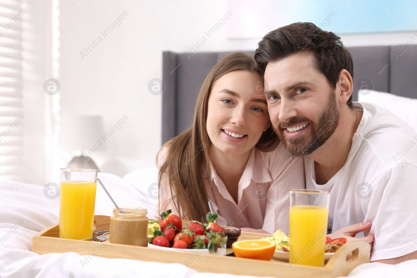 Photo of Family portrait of happy couple with tray of tasty breakfast on bed at home. Space for text