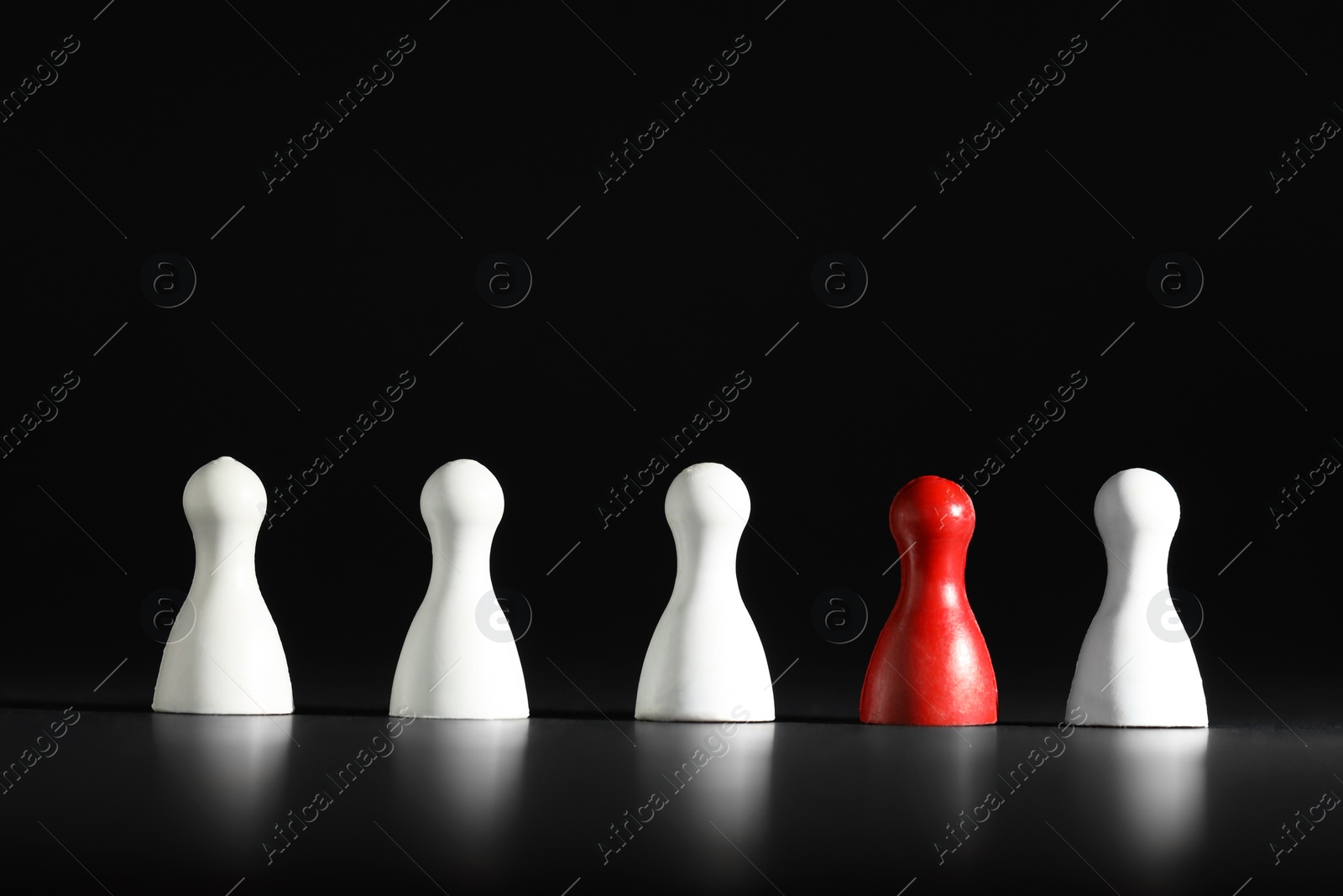 Photo of Choice concept. Red pawn among white ones on black table