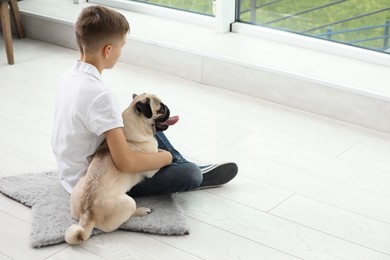 Photo of Boy with his cute pug on floor indoors. Space for text