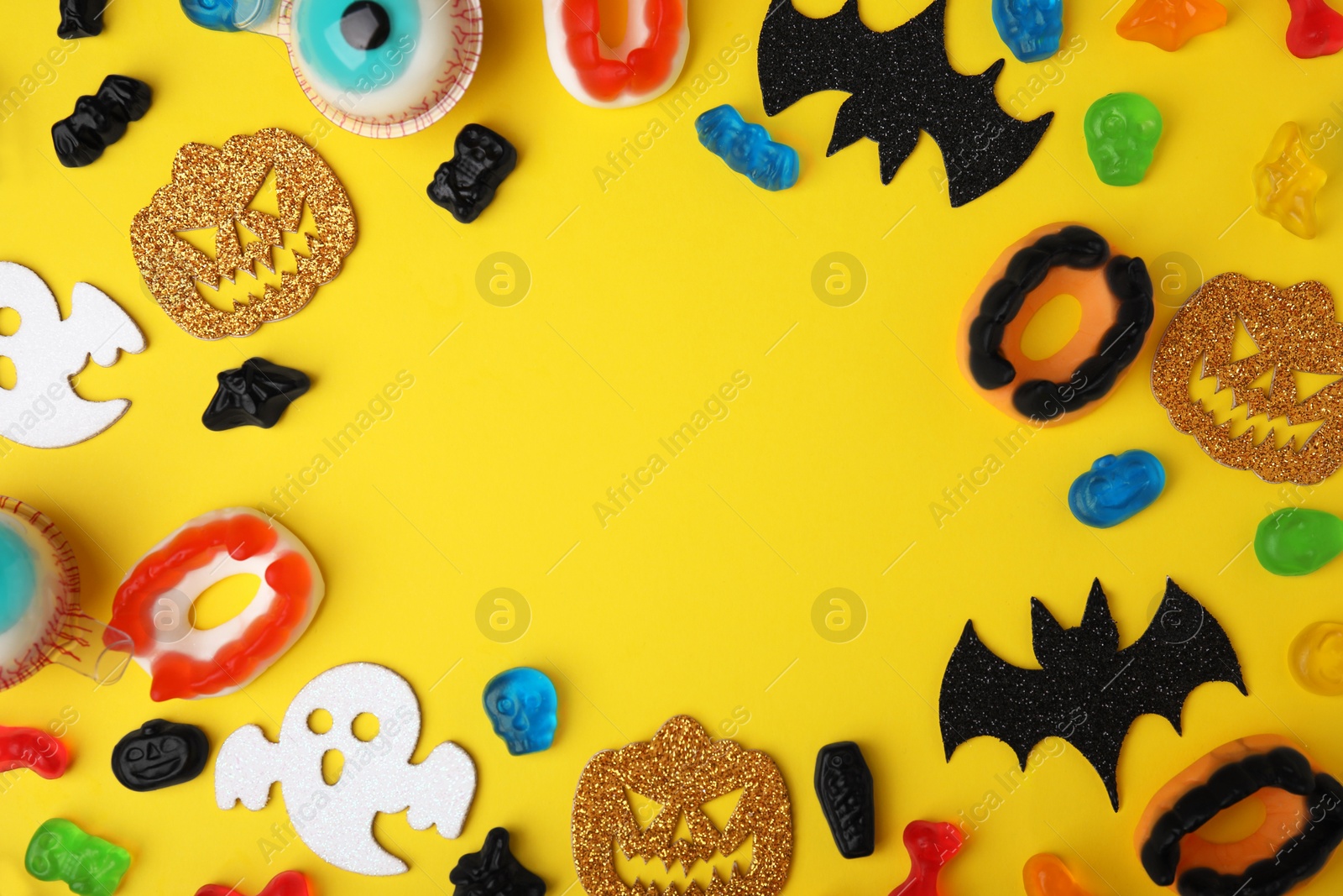 Photo of Frame made of tasty candies and Halloween decorations on yellow background, flat lay. Space for text