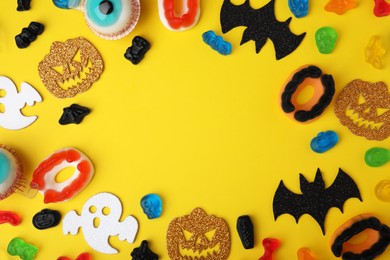 Frame made of tasty candies and Halloween decorations on yellow background, flat lay. Space for text