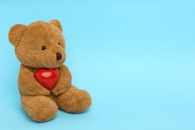Photo of Cute teddy bear with red heart on light blue background, space for text. Valentine's day celebration
