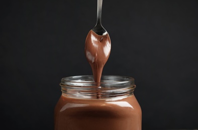 Photo of Pouring sweet chocolate cream into glass jar on dark background