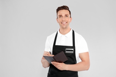 Photo of Handsome waiter in apron taking order on light background