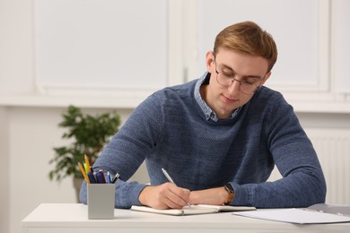 Photo of Young man writing in notebook at table indoors