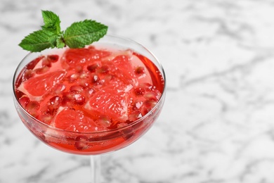 Glass of tasty refreshing cocktail with grapefruit and pomegranate on white marble table, closeup. Space for text