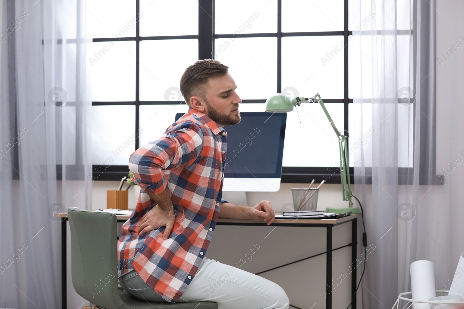 Photo of Young man suffering from back pain in office