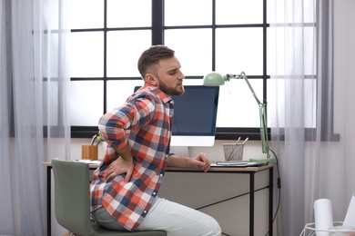 Photo of Young man suffering from back pain in office