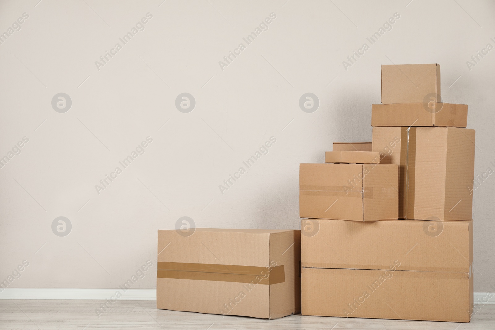 Photo of Pile of cardboard boxes near light wall indoors. Space for text