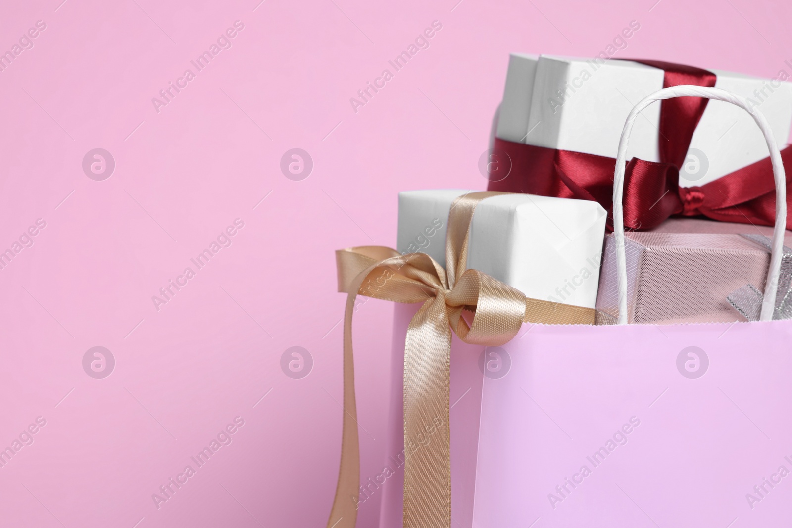 Photo of Color paper shopping bag full of gift boxes on pink background. Space for text