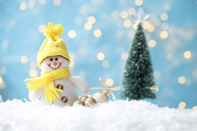 Photo of Snowman toy and Christmas balls on snow against blurred festive lights. Space for text