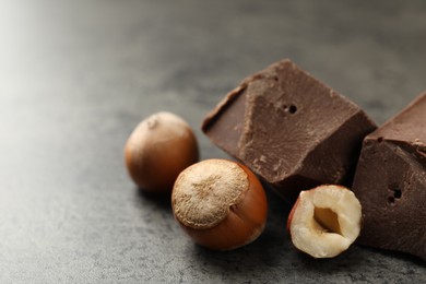 Delicious chocolate chunks and hazelnuts on grey table, closeup. Space for text