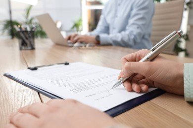 Woman signing contract at table in office, closeup.