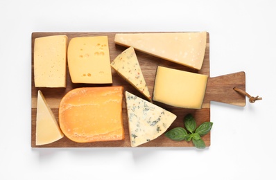 Photo of Wooden board with different kinds of cheese and basil on white background, top view