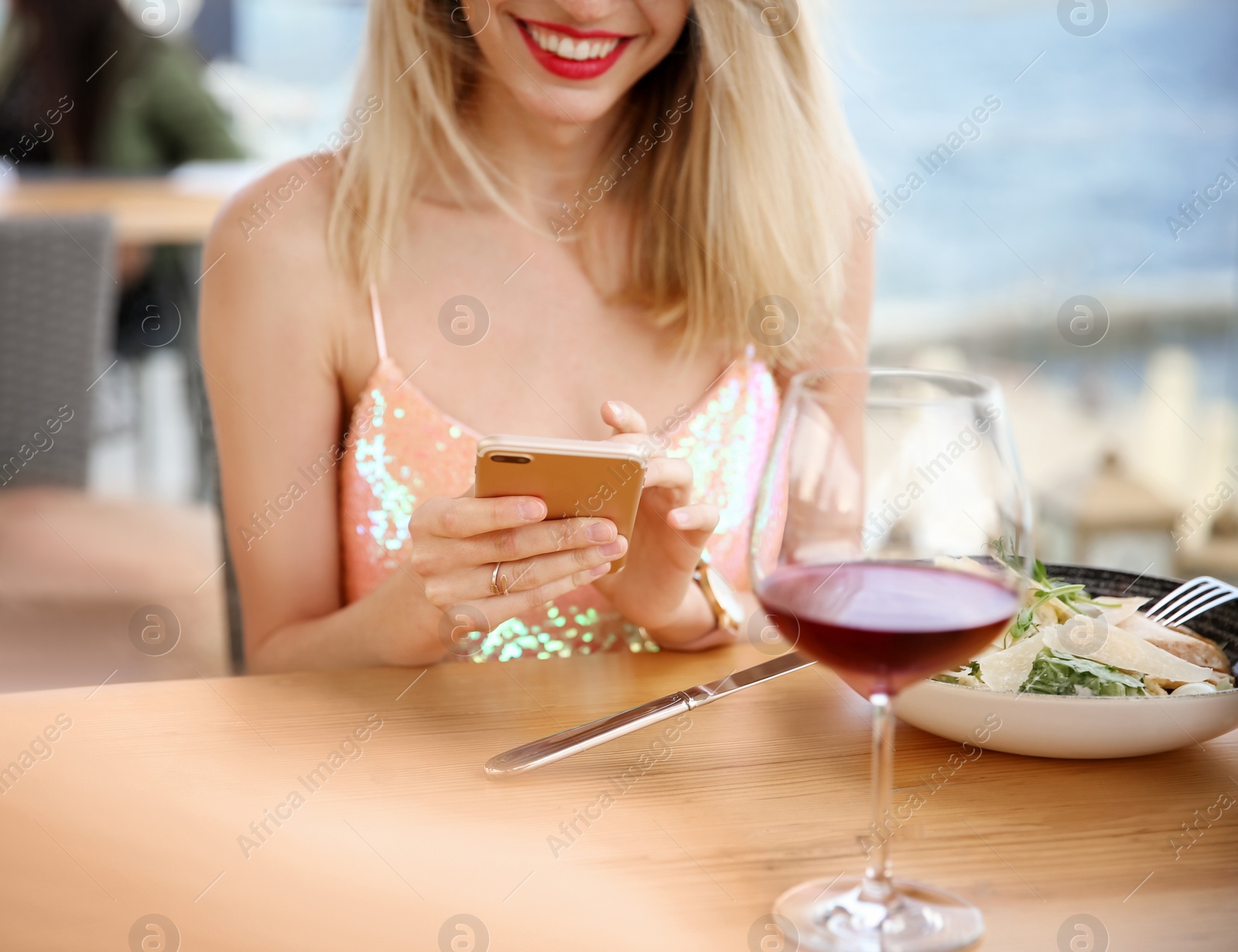 Photo of Young woman with smartphone and glass of wine at table