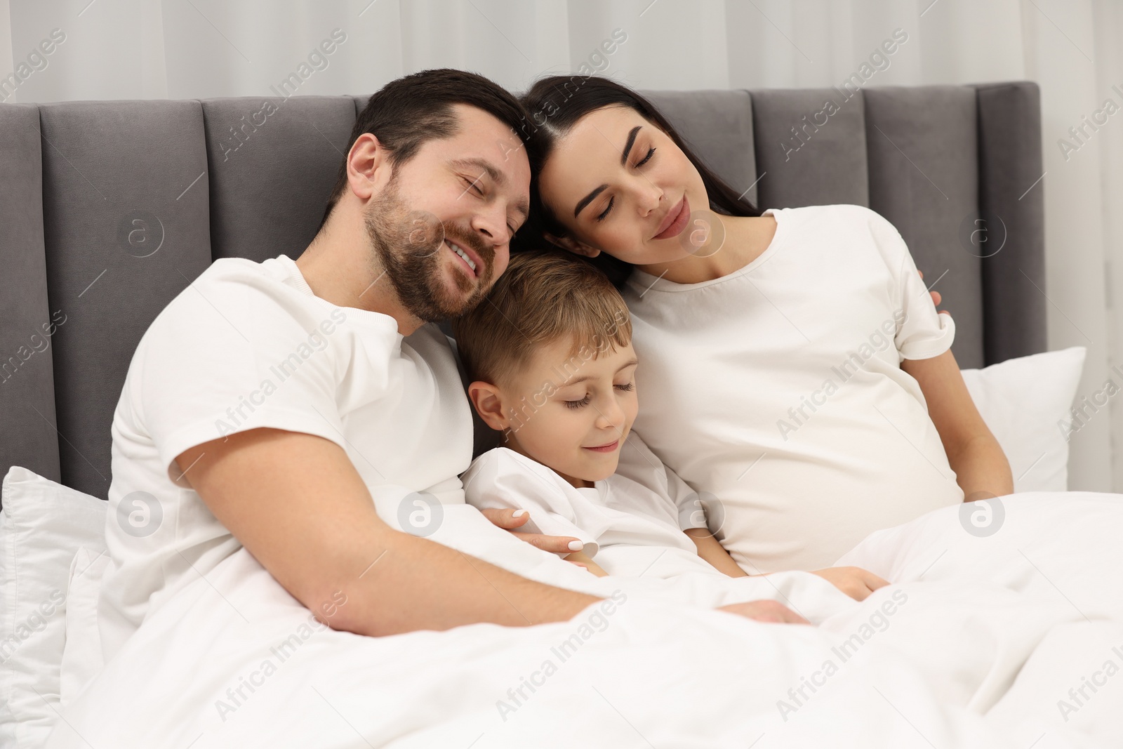 Photo of Pregnant woman with her son and husband in bed at home. Cute family