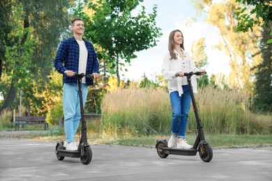 Happy couple riding modern electric kick scooters in park