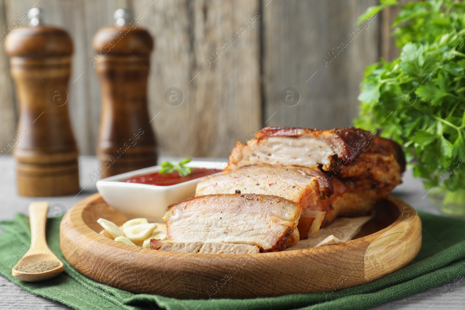 Photo of Pieces of baked pork belly served with sauce on grey wooden table, closeup