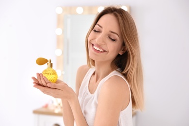 Photo of Young woman with bottle of perfume near mirror indoors