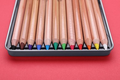 Photo of Box with many colorful pastel pencils on red background, closeup. Drawing supplies