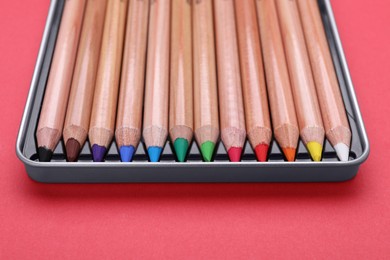 Box with many colorful pastel pencils on red background, closeup. Drawing supplies