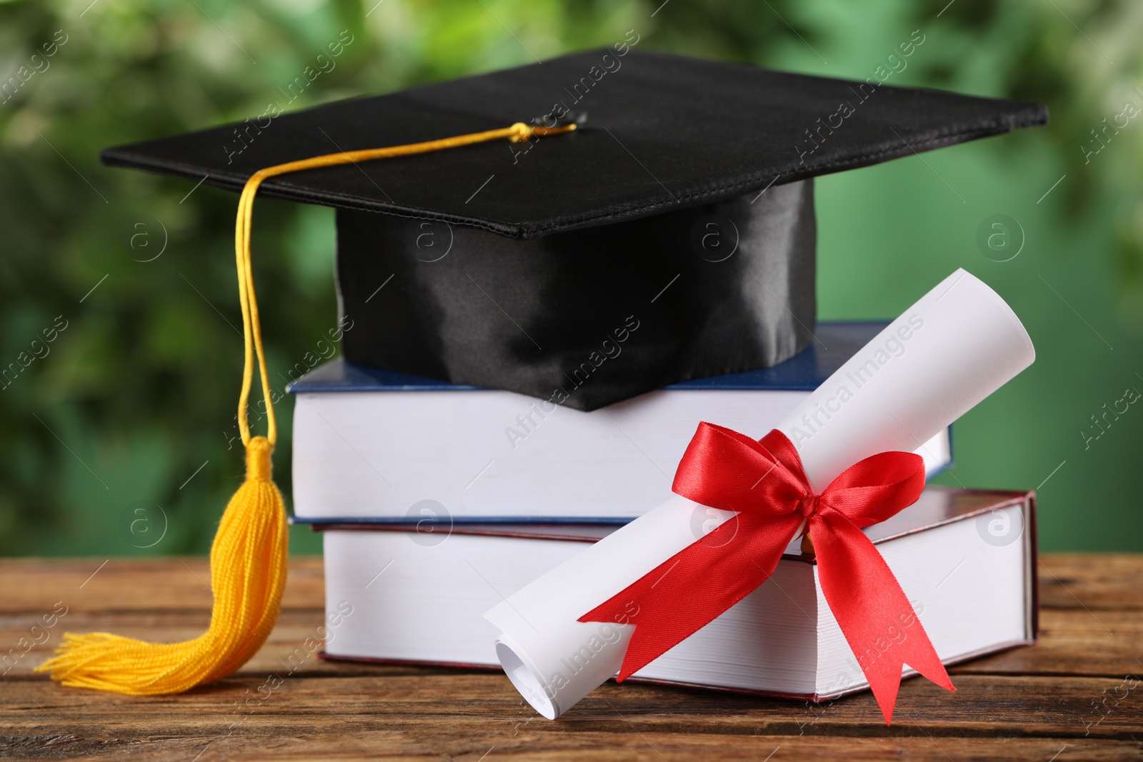 Photo of Graduation hat, books and diploma on wooden table against blurred background