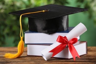 Photo of Graduation hat, books and diploma on wooden table against blurred background