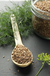 Photo of Spoon with dry seeds and fresh dill on black table, selective focus. Space for text