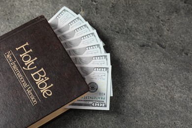Photo of Holy Bible and money on grey table, top view. Space for text