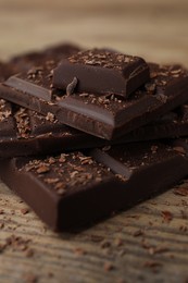 Photo of Pieces and shavings of tasty chocolate on wooden table, closeup
